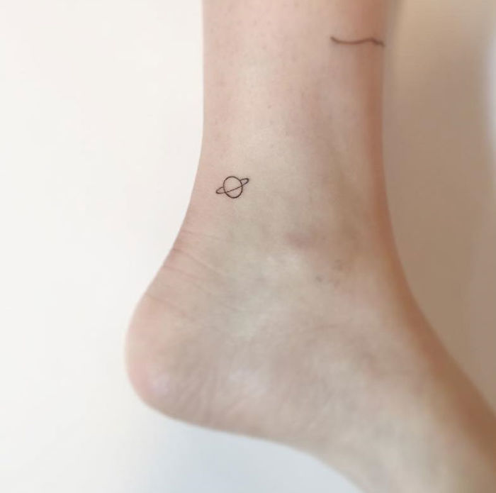 Minimalist tattoo of a planet on an ankle by Korean artist.