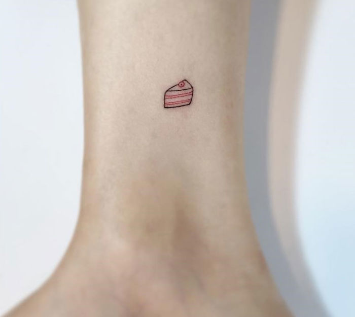 Minimalist tattoo of a tiny cake slice on ankle by Korean artist.