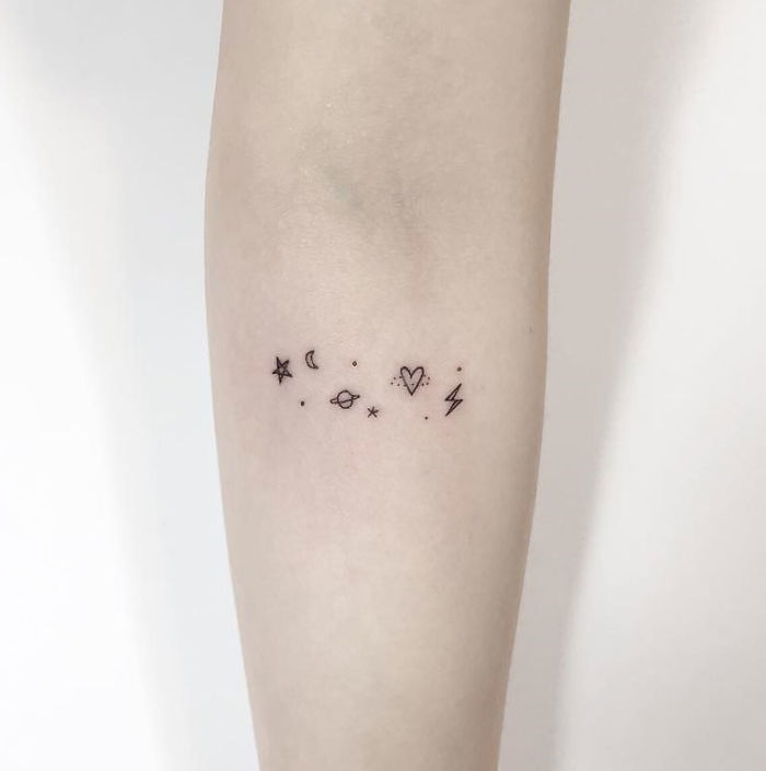 Minimalist tattoo with star, moon, planet, heart, and lightning symbols on a forearm by a Korean artist.