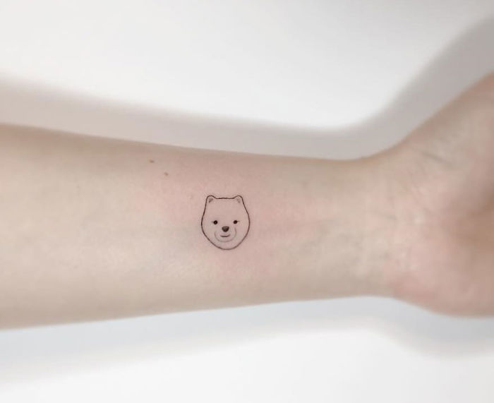 Minimalist tattoo of a bear's face on a person's forearm by a Korean artist.