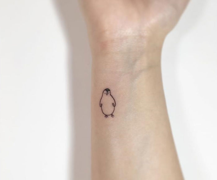 Minimalist tattoo of a small penguin on a wrist by Korean artist.