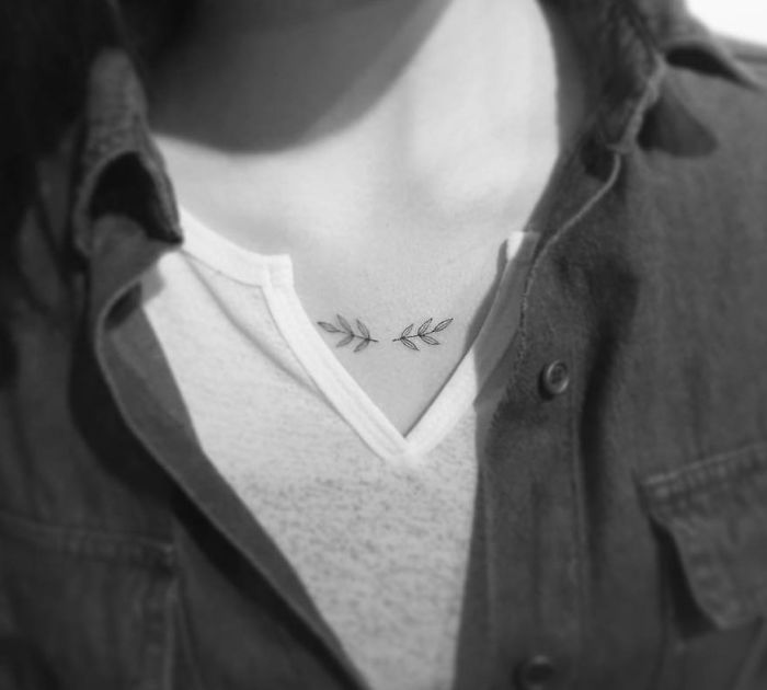 Minimalist tattoo design on a person's chest with leaf motifs, created by a Korean artist.