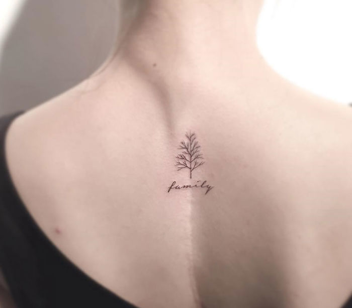 Minimalist tattoo of a tree with the word "family" on a person's upper back by a Korean artist.
