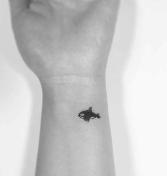 Minimalist tattoo of a small orca on a wrist, designed by a Korean artist.