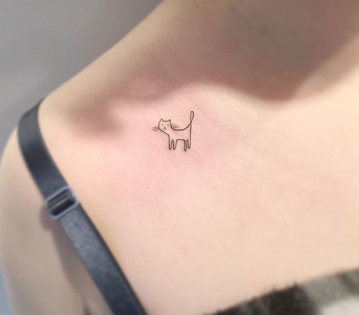 Minimalist tattoo of a small cat on shoulder by a Korean artist.
