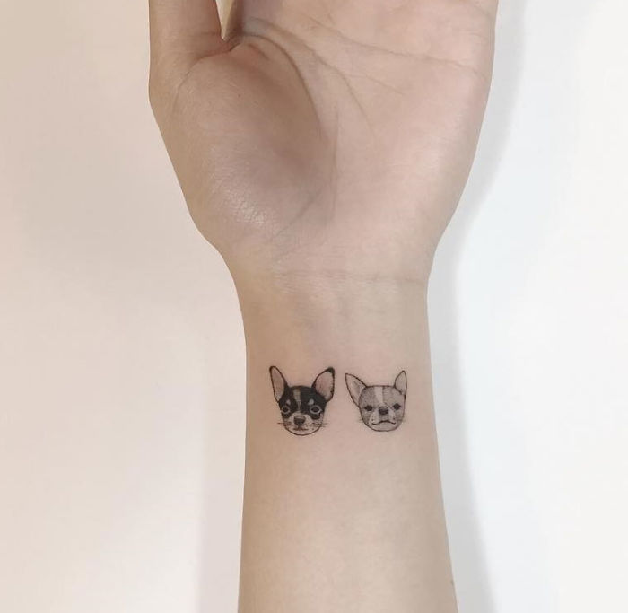 Minimalist tattoos featuring two small dog faces on a person's wrist by a Korean artist.