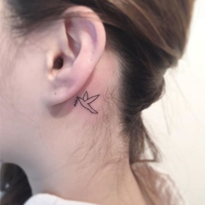 Minimalist tattoo of a hummingbird behind the ear, designed by a Korean artist.