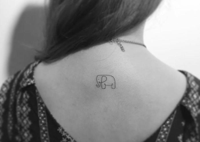 Minimalist tattoo of a small elephant on a woman's upper back, designed by a Korean artist.