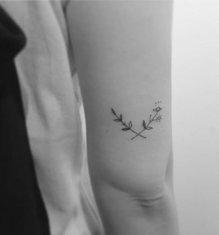 Minimalist tattoo of crossed branches on a person's arm by a Korean artist.