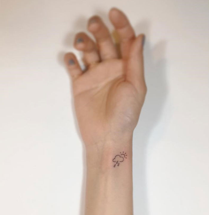 Minimalist tattoo of a cloud with rain and sun on a wrist by Korean artist.