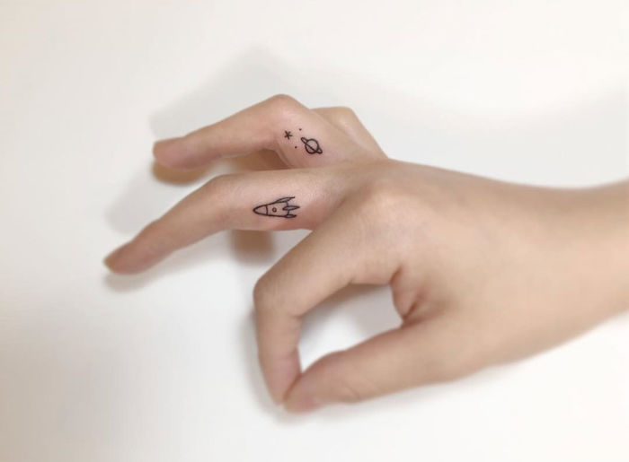 Minimalist tattoos of a rocket and planets on fingers by a Korean artist.