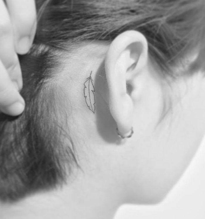 Minimalist tattoo of a feather behind the ear by a Korean artist.