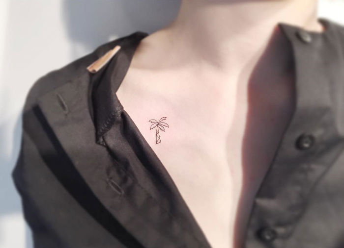 Minimalist palm tree tattoo on a collarbone, designed by a Korean artist, with a partially unbuttoned black shirt.