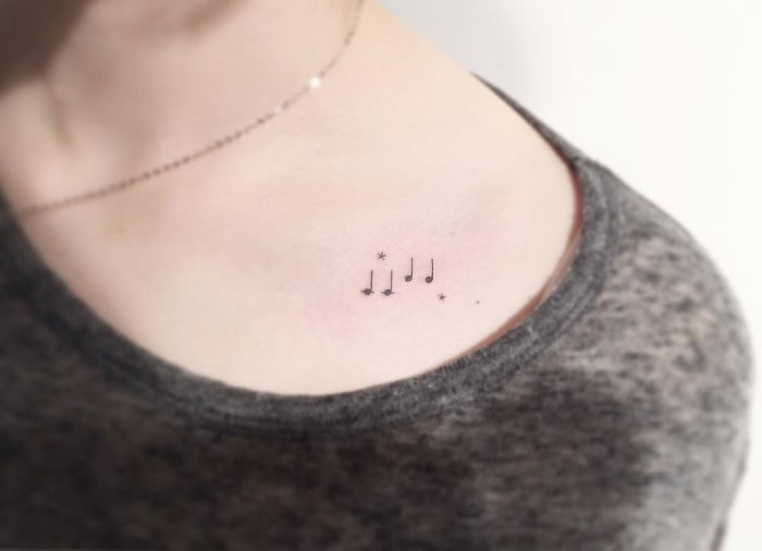 Minimalist tattoo of musical notes and stars on a person's upper chest, designed by a Korean artist.