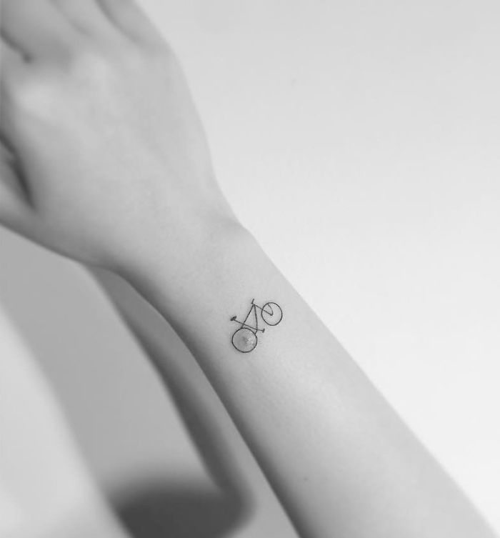 Minimalist tattoo of a small bicycle on a person's forearm by Korean artist.