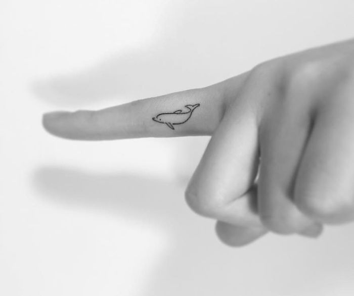 Minimalist tattoo of a whale on a finger, created by a Korean artist.