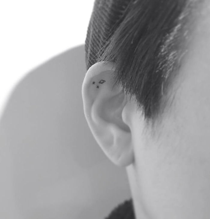 Minimalist tattoo of stars and an infinity symbol on the inner ear, designed by a Korean artist.