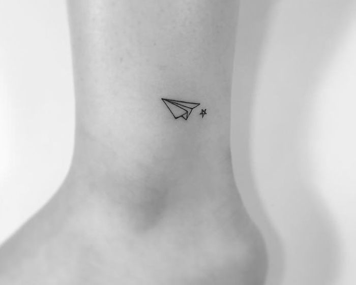 Minimalist tattoo of a paper plane and star on an ankle by a Korean artist.