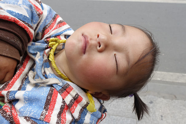 Child From Tibet Napping On The Back Of Her Mother While She Is Walking.