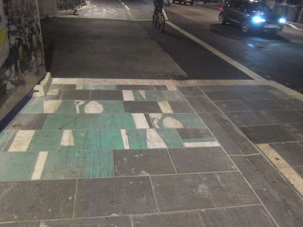 Failed road marking job on a sidewalk at night, misaligned tiles disrupting the pattern.