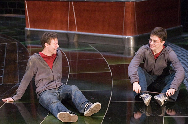 Two men in casual clothes sitting on a shiny floor, demonstrating Hollywood celebrities body doubles in a staged setting.
