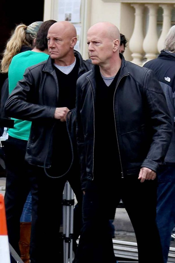 Hollywood scene with a celebrity and body double wearing black leather jackets on a busy film set outdoors.
