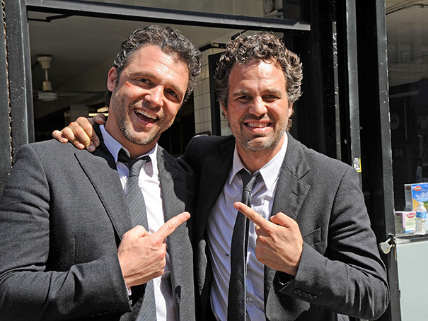 Two men in black suits smiling and pointing at each other, illustrating celebrities’ body doubles concept.
