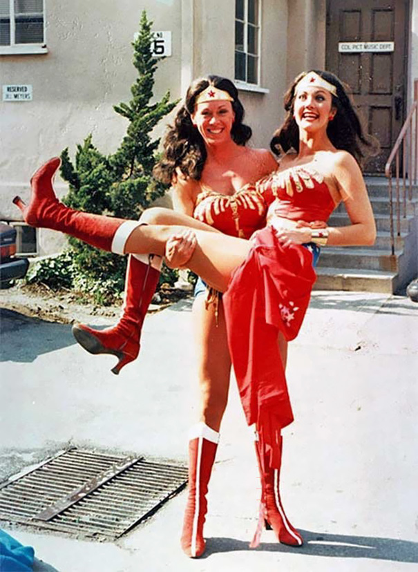 Two women dressed as Wonder Woman, one lifting the other, illustrating Hollywood celebrities’ body doubles on set.