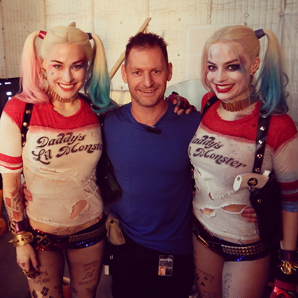 A man posing with two women dressed as Harley Quinn, showcasing Hollywood celebrities’ body doubles on set.
