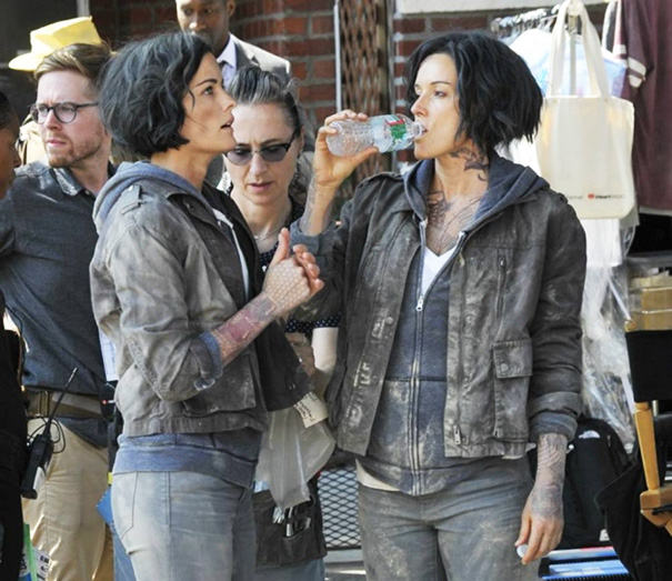 Two women with tattoos and short dark hair dressed as celebrities with body doubles on a Hollywood film set.