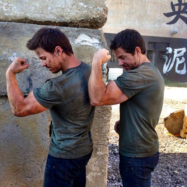 Two men wearing green shirts flexing muscles back-to-back, showcasing Hollywood celebrity body doubles on set.