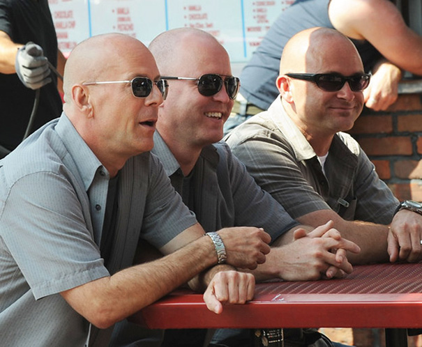 Three men wearing sunglasses and gray shirts sitting side by side, illustrating Hollywood celebrities’ body doubles concept.
