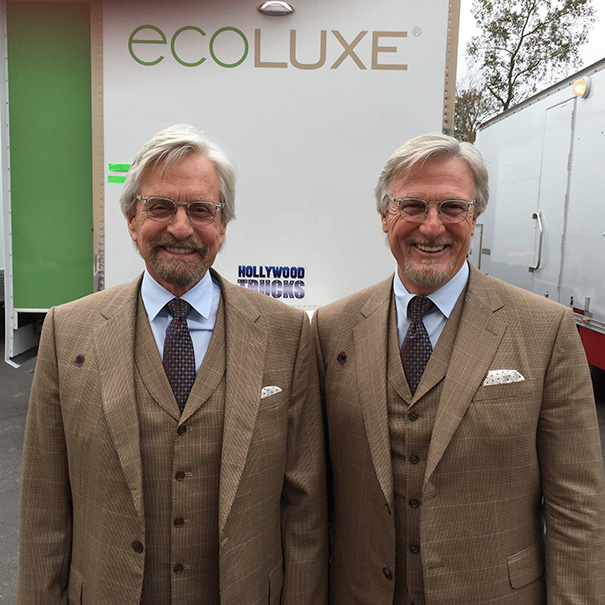 Two men dressed as identical celebrities, serving as Hollywood body doubles on a movie set, smiling outdoors.