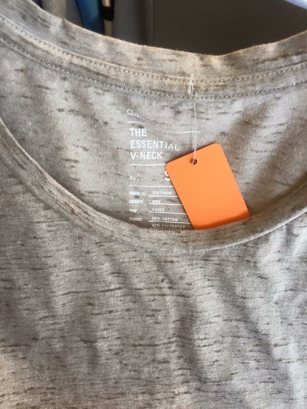 A V-neck shirt with "THE ESSENTIAL V-NECK" label, featuring a hang tag that mistakenly obstructs the view.