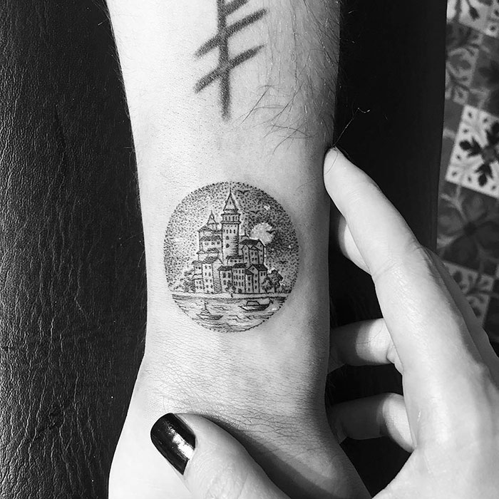 Miniature circle tattoo of a castle on a wrist, done by Turkish artist Eva Krbdk.
