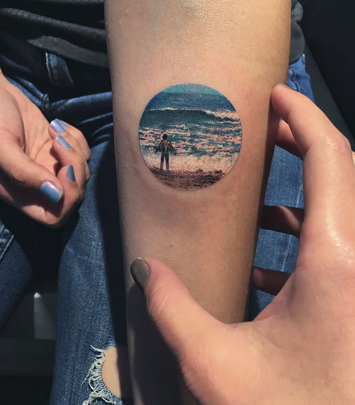 Person displaying a miniature circle tattoo of a seaside scene by Turkish artist.