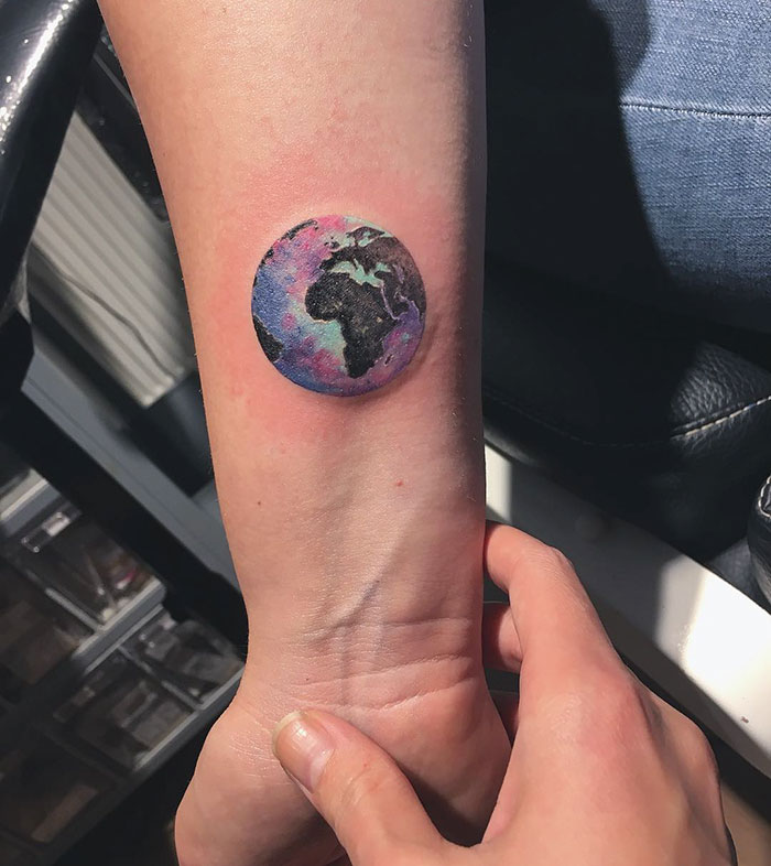 Colorful miniature circle tattoo by Turkish artist Eva Krbdk on a forearm, displaying a world map design.
