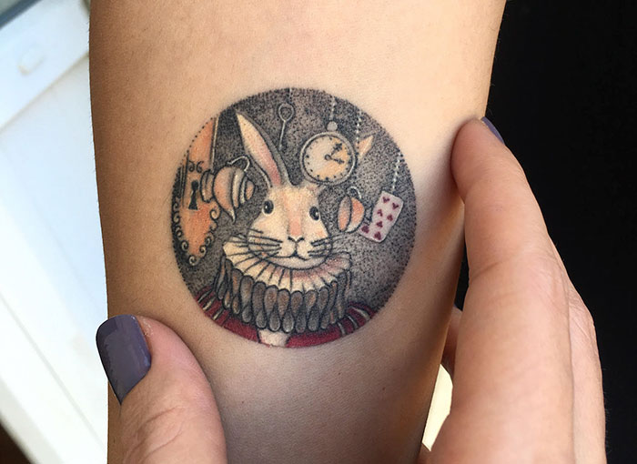 Miniature circle tattoo by Turkish artist Eva Krbdk featuring a detailed rabbit with a clock and playing card.
