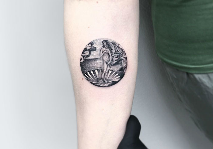 Miniature circle tattoo by Turkish artist Eva Krbdk featuring a detailed black and gray design on an arm.