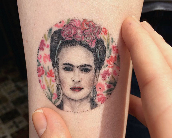 Miniature circle tattoo of a woman with floral background by Turkish artist Eva Krbdk on a person's arm.