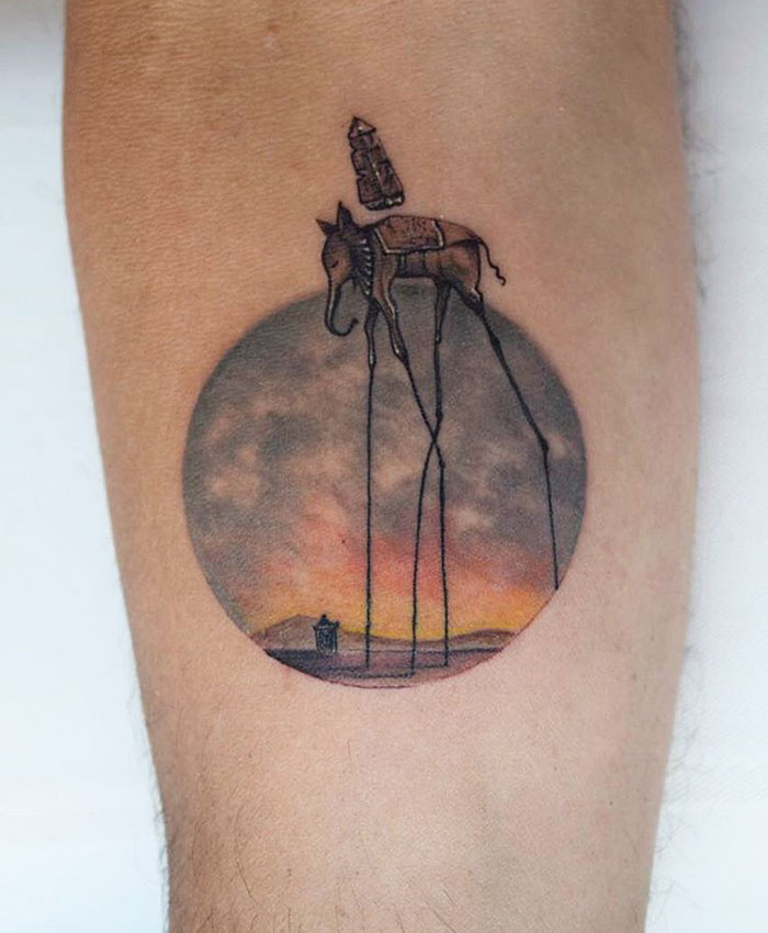 Miniature circle tattoo by Eva Krbdk featuring a surreal elephant with long legs, set against a sunset scene.