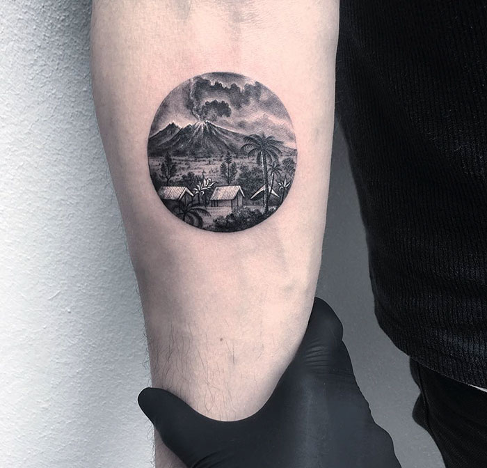 A circular tattoo of a landscape with a volcano by Turkish artist Eva Krbdk on an arm.