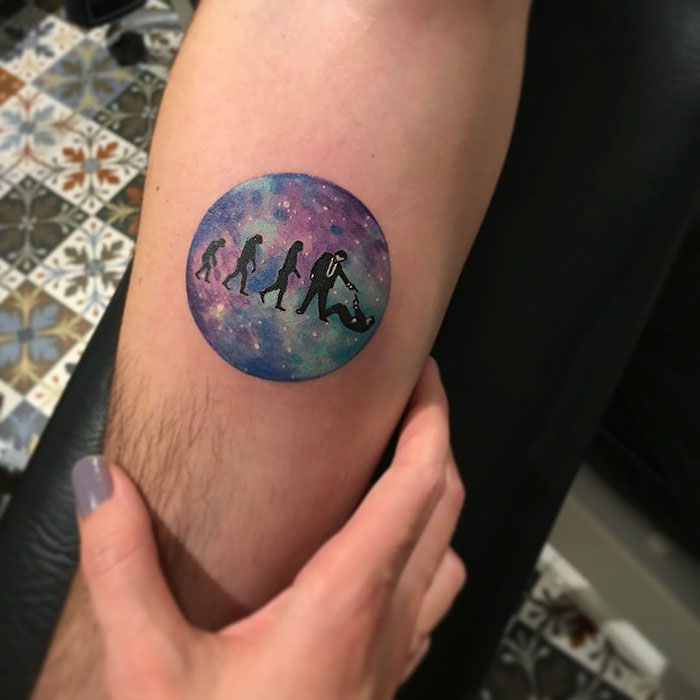 Miniature circle tattoo of evolutionary silhouettes on a colorful backdrop by Turkish artist Eva Krbdk.