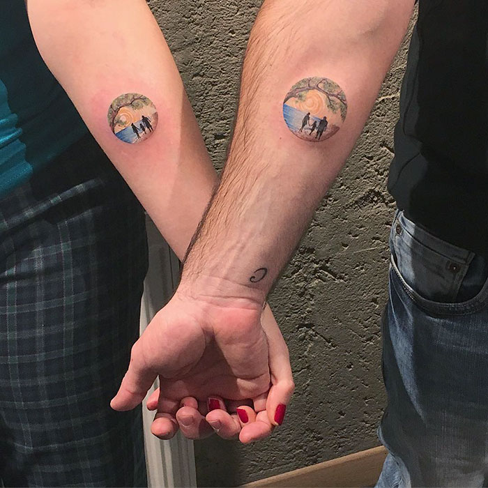 Two arms with matching miniature circle tattoos by Turkish artist Eva Krbdk, depicting a scenic landscape.