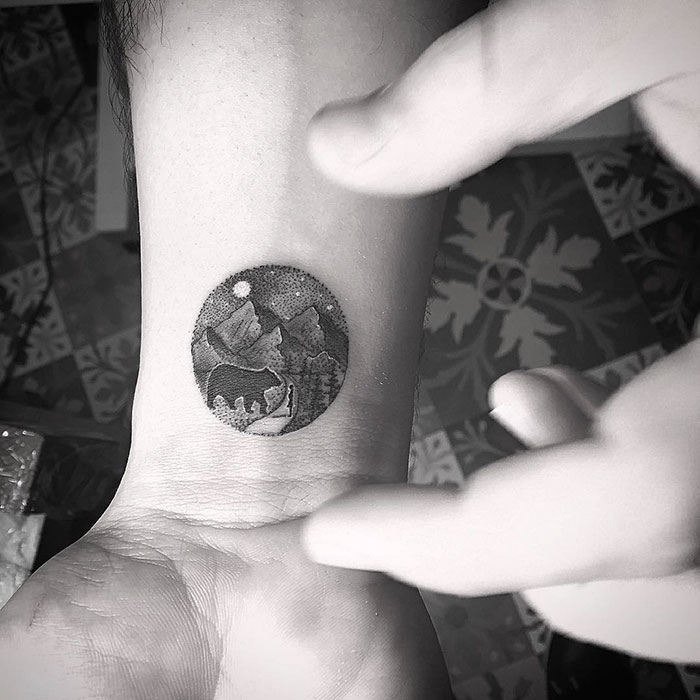 Miniature circle tattoo of a mountain landscape on a wrist, designed by Turkish artist Eva Krbdk.