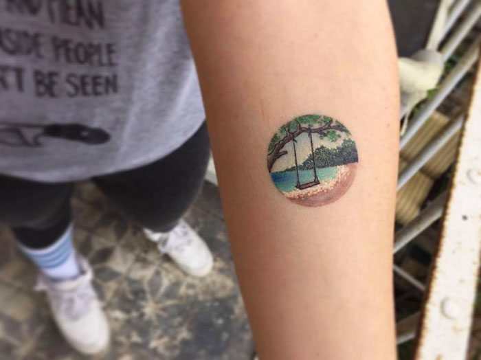 Miniature circle tattoo featuring a beach scene with a swing, designed by Turkish artist Eva Krbdk.