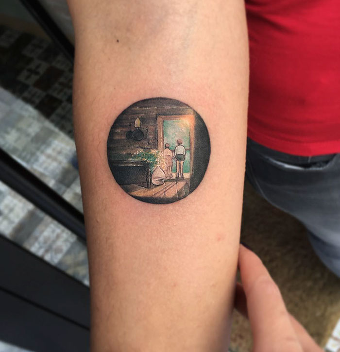 Miniature circle tattoo by Turkish artist Eva Krbdk featuring a detailed indoor scene on forearm.