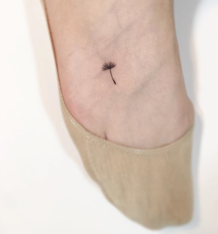 Minimalist tattoo of a small dandelion seed on an ankle by a Korean artist.