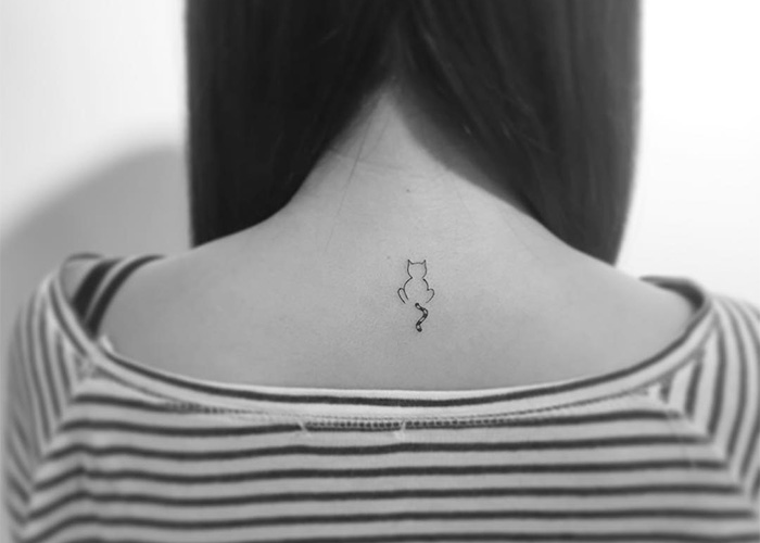 Minimalist tattoo of a small cat on the back of a person wearing a striped shirt, designed by a Korean artist.