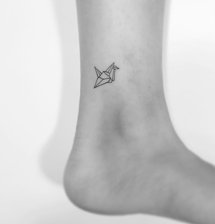 Minimalist tattoo of an origami crane on an ankle by a Korean artist.